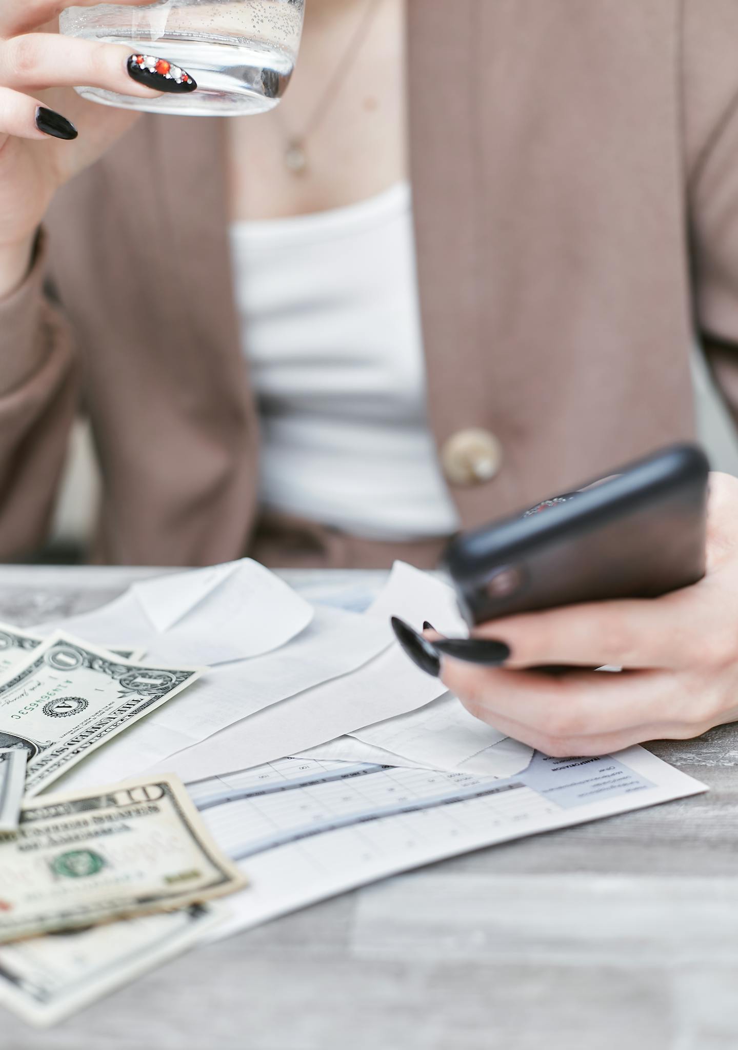 Close-up of a woman using a smartphone, holding cash, and managing finances indoors.